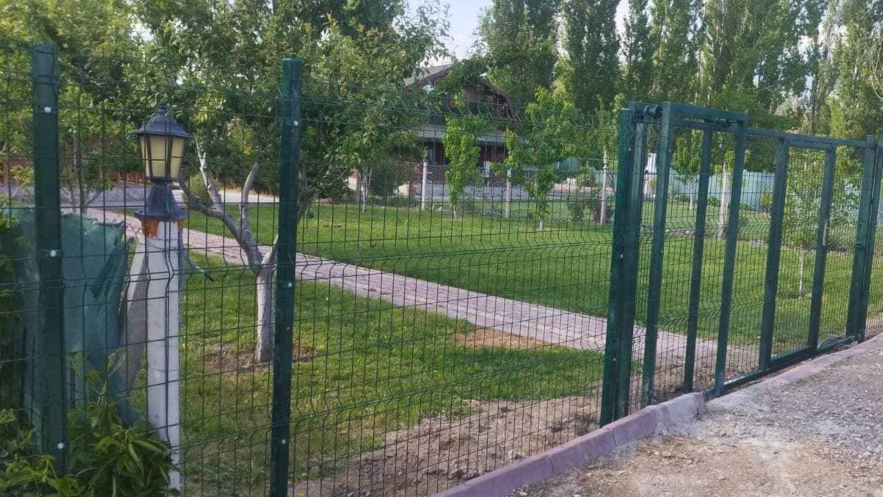 Yeşil alan çevresinde aydınlatma direği boyunca uzanan panel çit hattı